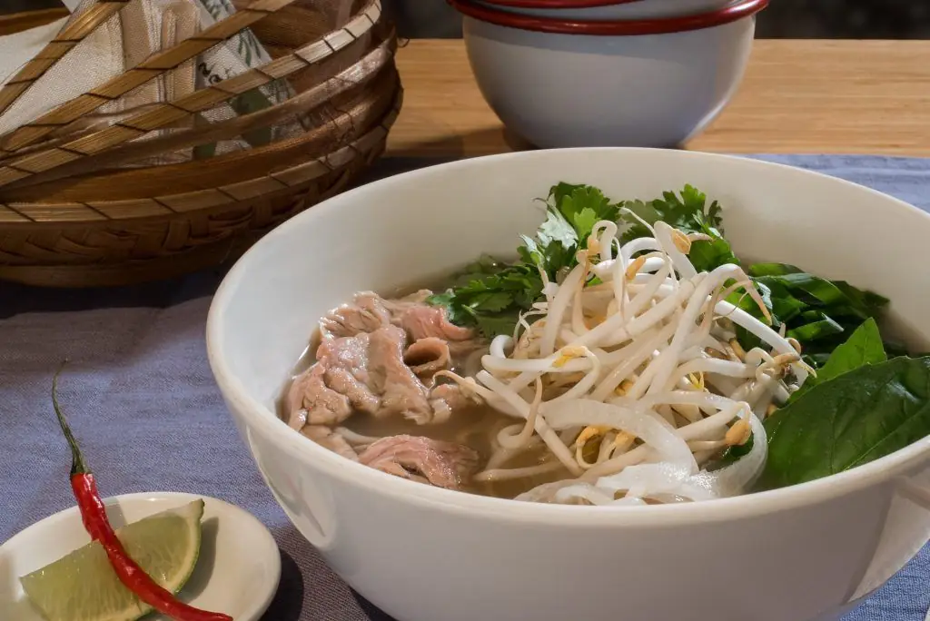 Bowl of pho with sliced beef, rice noodles, bean sprouts, herbs, lime and a red chili on the side, La Vietnamita