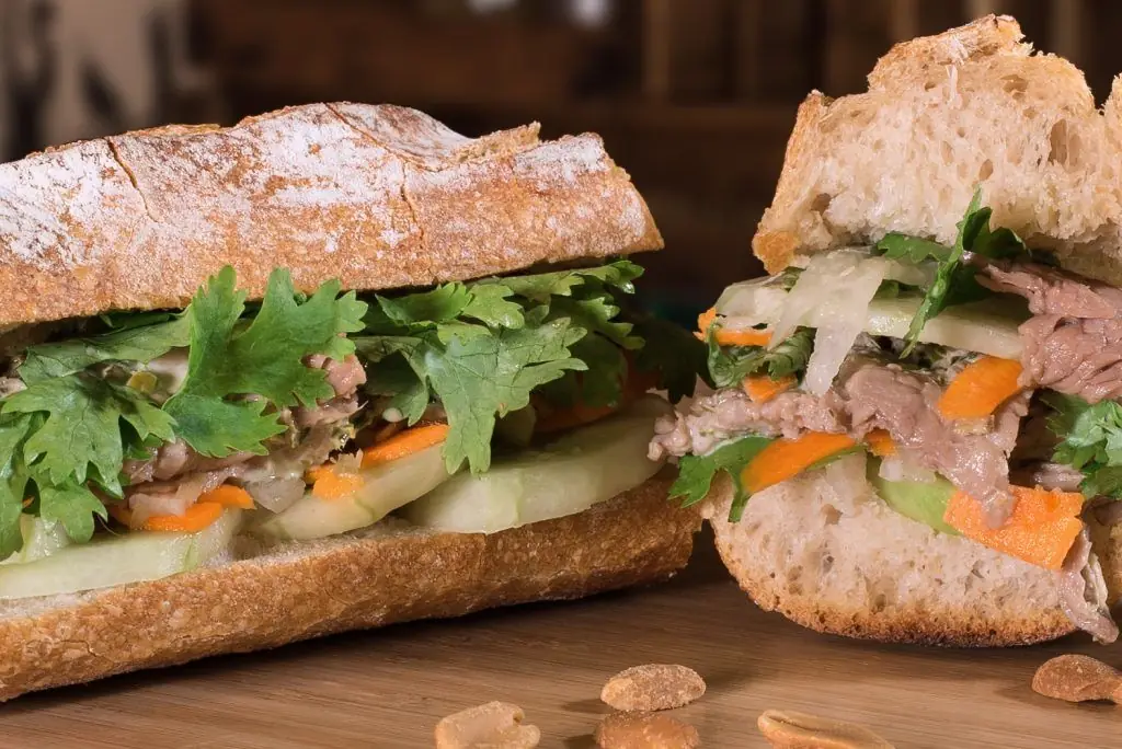 Vietnamese banh mi baguette sandwich sliced open, filled with meat, cucumber, carrot and cilantro, La Vietnamita