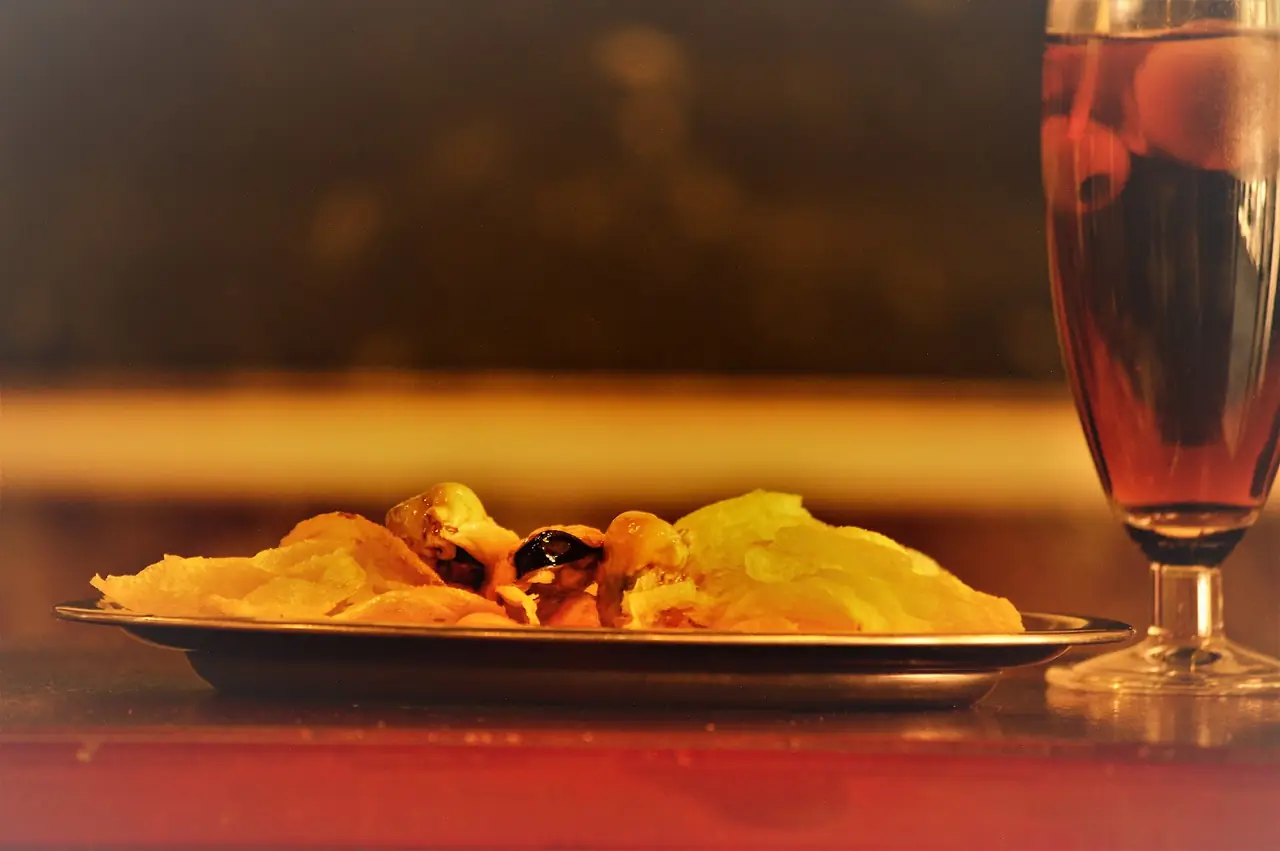 Plate of potato chips with pickled mussels beside a glass of vermut