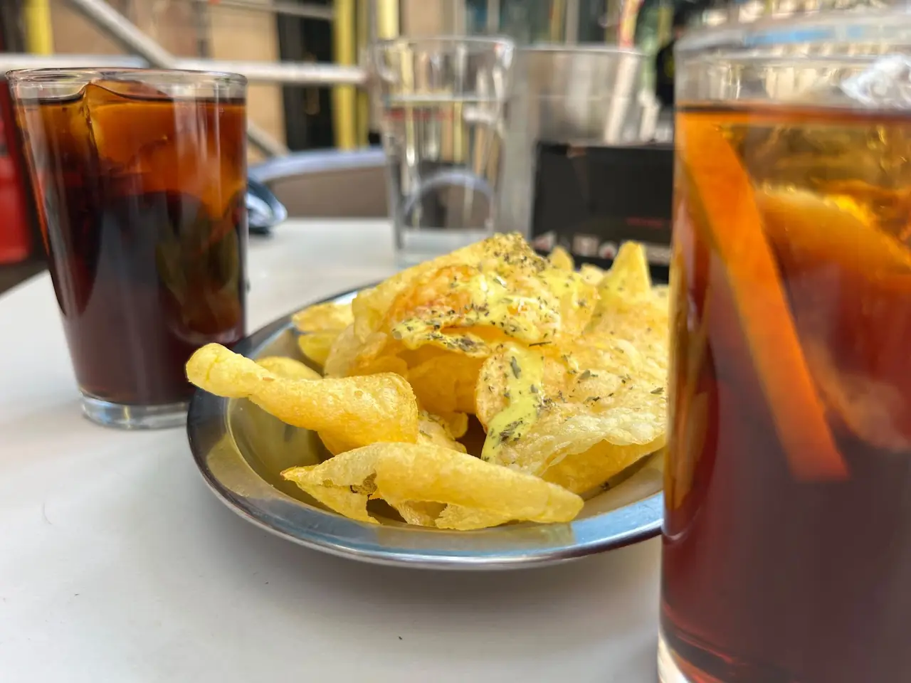 Plate of potato chips topped with sauce and herbs, served alongside vermut on the rocks