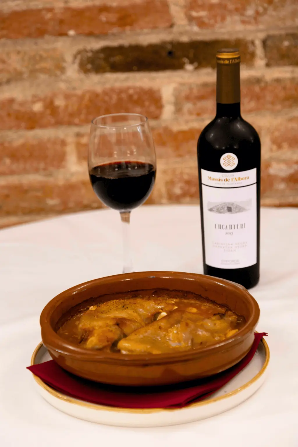 Braised meat in sauce served in a terracotta cazuela dish, with a glass of red wine, La Yaya Amelia