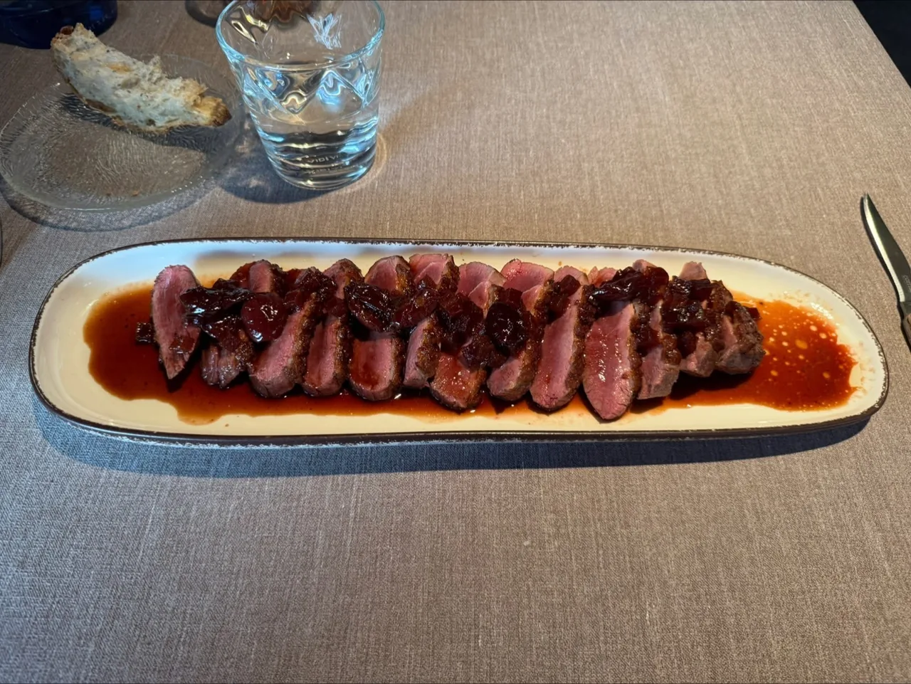 Sliced duck breast in a red sauce on a long oval plate on a linen table