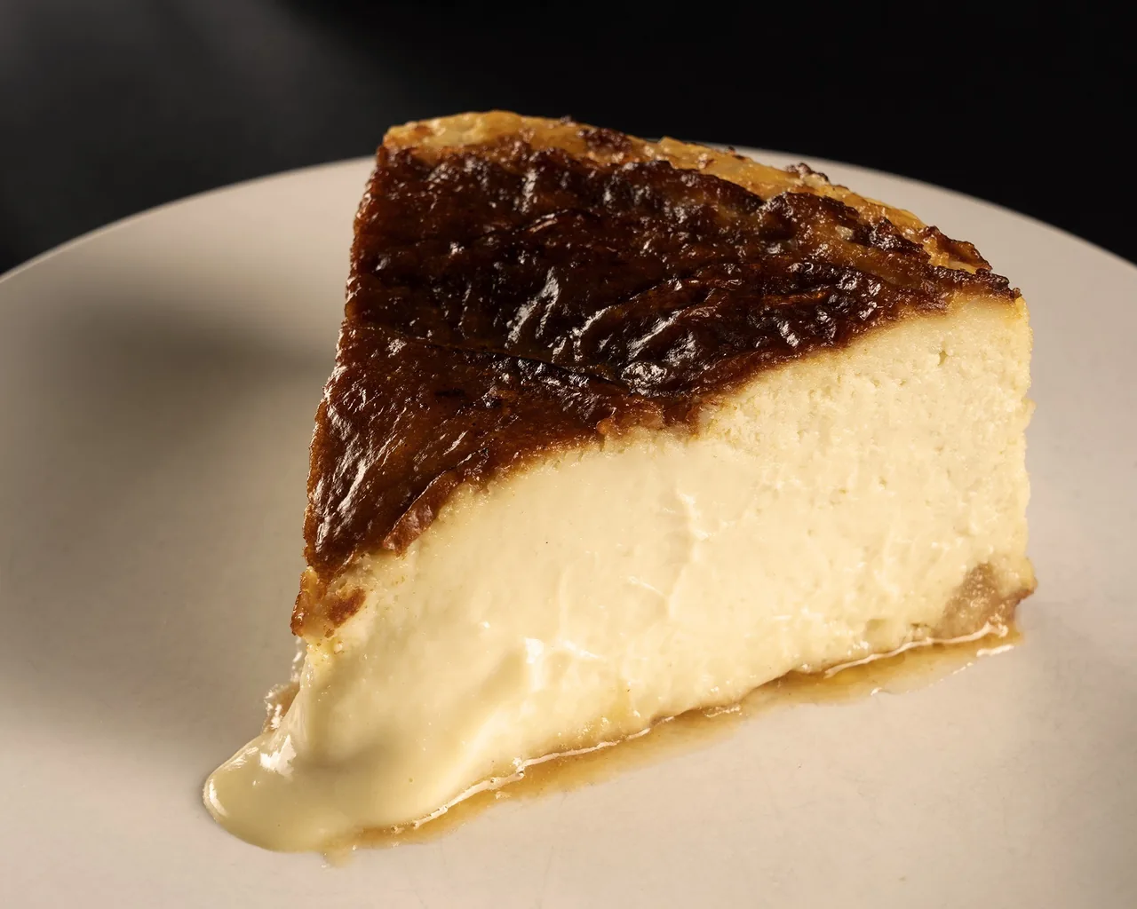 A slice of cheesecake with a dark caramelised top on a white plate
