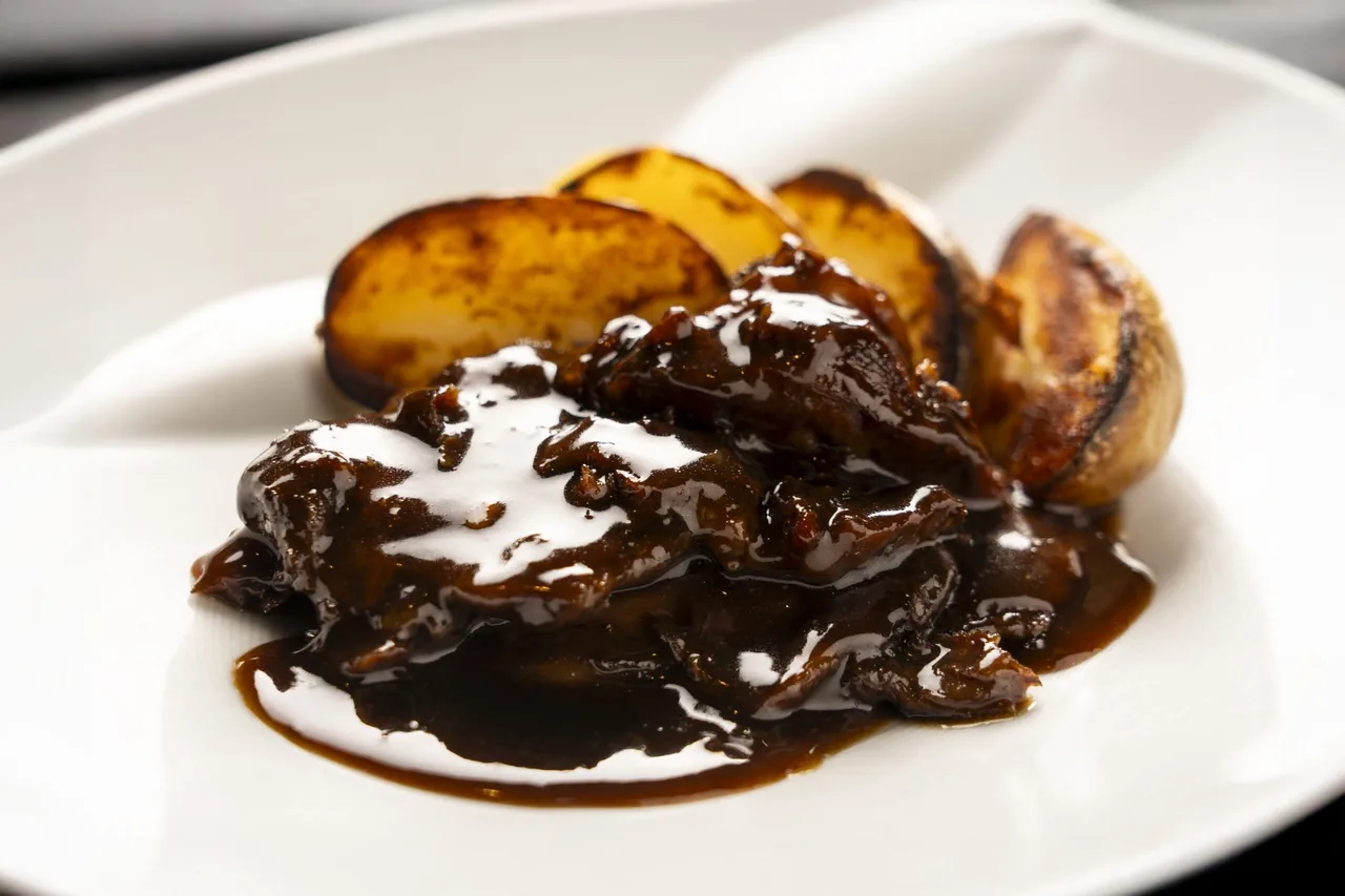 A dish with glossy dark sauce and roasted potato wedges on a white plate