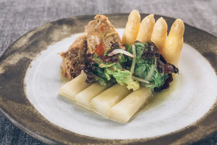 Plate of white asparagus spears with shredded braised meat and a mixed leaf salad