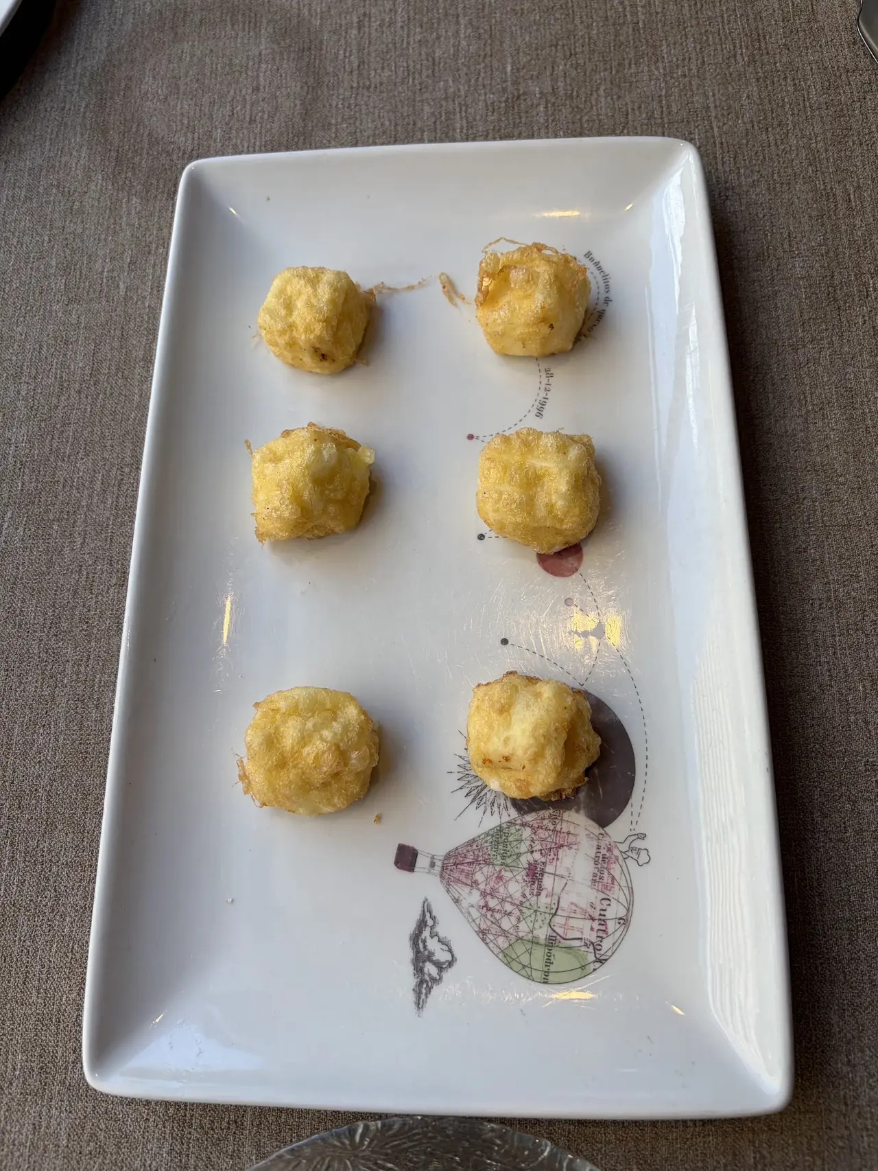 Six golden fried croquettes arranged on a decorative rectangular plate