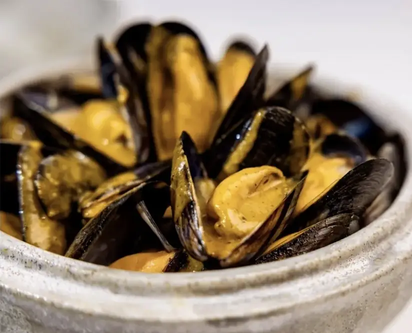 Close-up bowl of mussels in a creamy orange sauce
