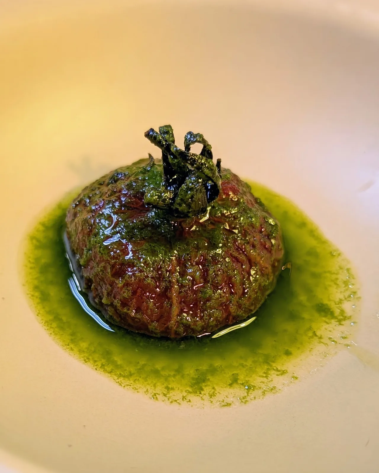 A round dish in a bright green sauce topped with a small dark garnish