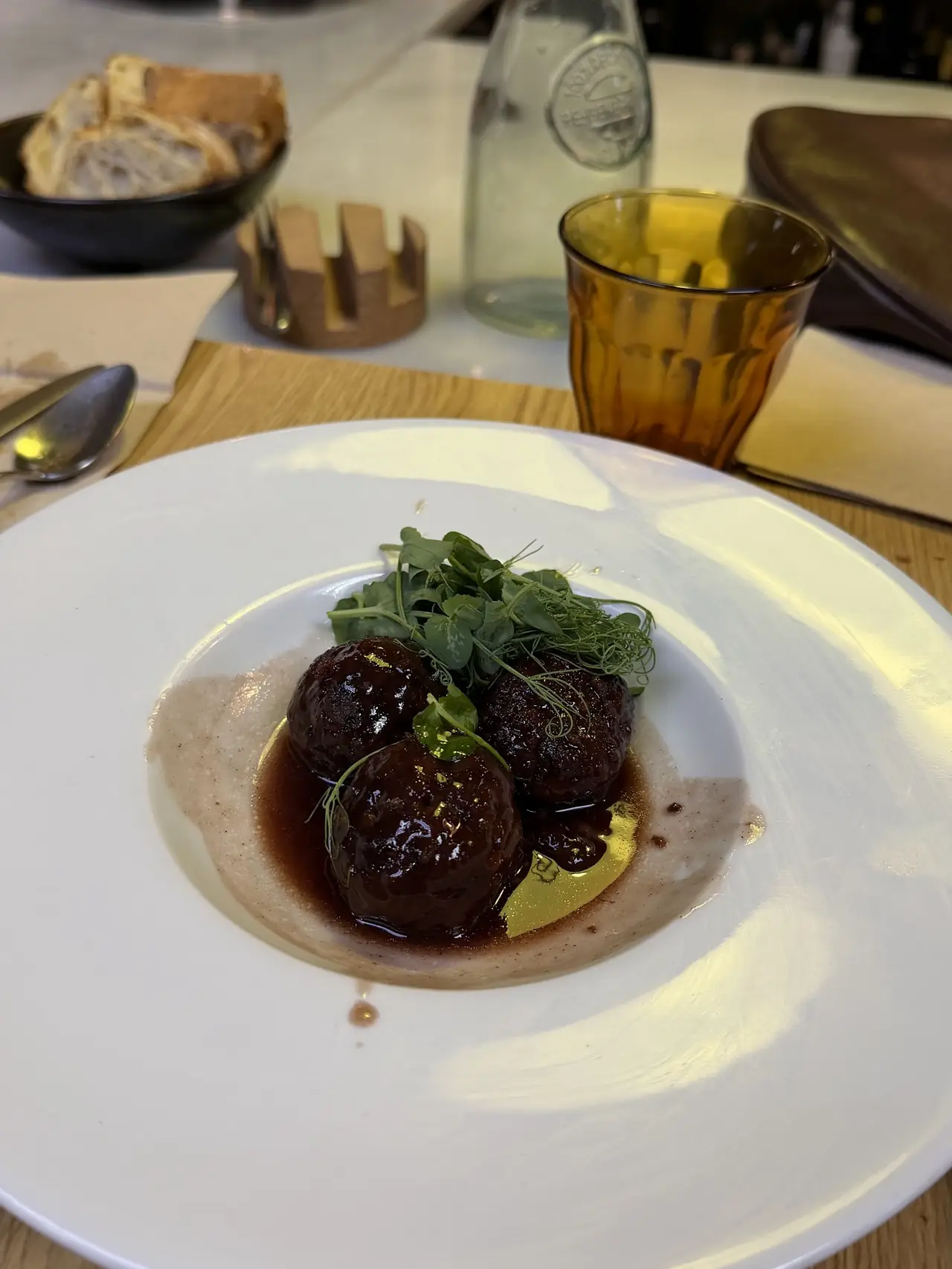 Three glazed meatballs on a cream sauce with dark reduction and micro greens on a white plate