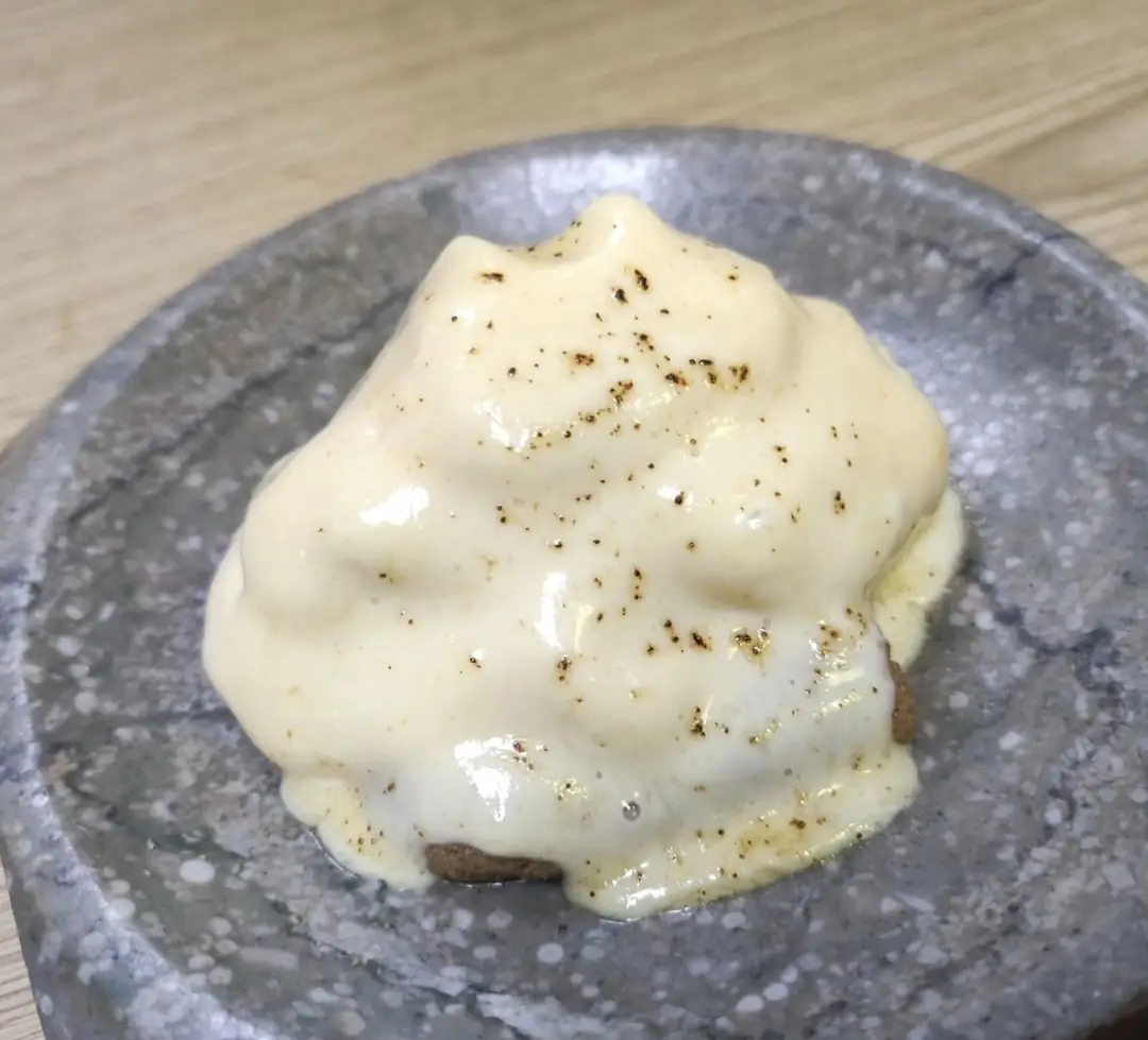 A dish smothered in a creamy sauce with black pepper flecks on a speckled stone plate