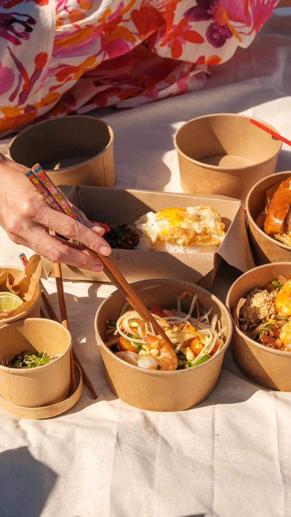Takeout containers of papaya salad with shrimp, fried rice, and a fried egg over rice, eaten with chopsticks outdoors, Lamai Thai Tapas