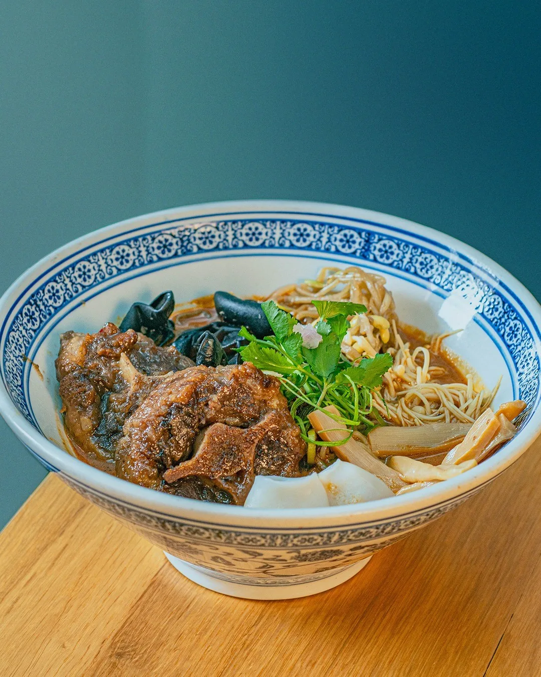 A blue and white patterned bowl of noodle soup with slices of braised meat and greens