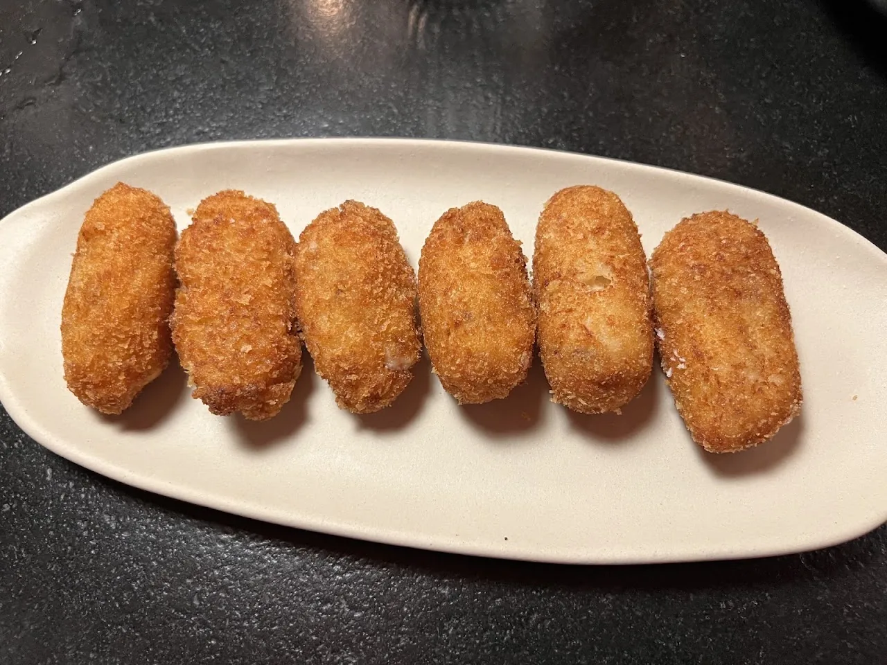 Six breaded croquettes on an oval plate