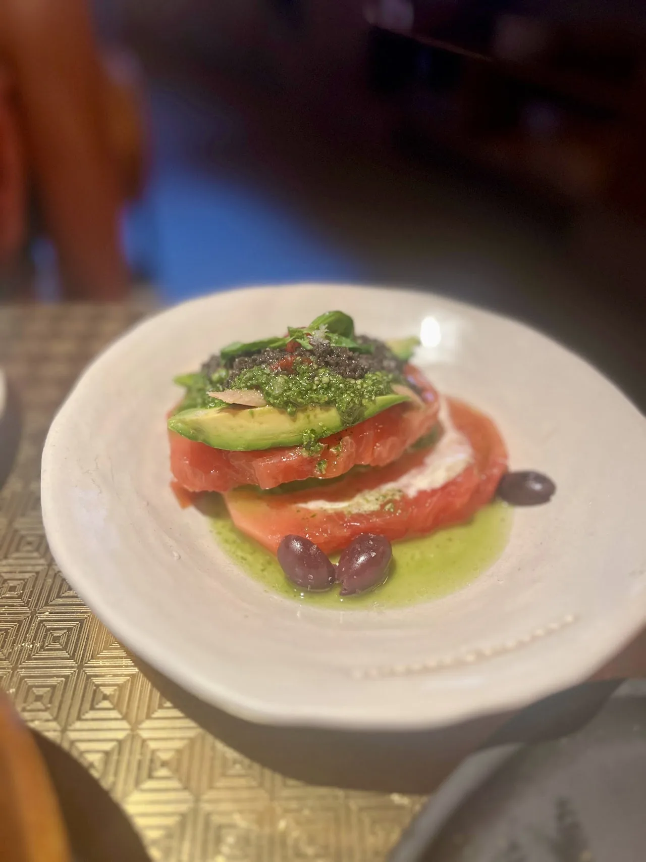 A plated salad of sliced tomato and avocado with greens