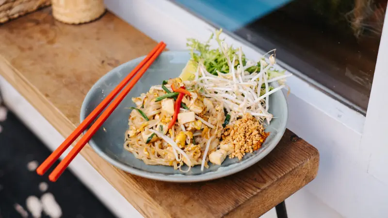 Pad Thai noodles with tofu, bean sprouts, and crushed peanuts on a plate with red chopsticks, at Lamun Cuina Thai