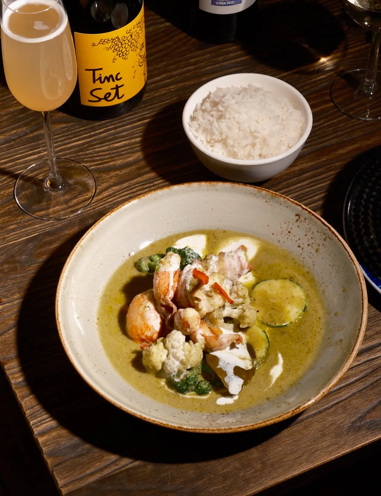 Shrimp green curry with cauliflower, zucchini, and broccoli in a ceramic bowl, served with a bowl of rice, at Lamun Cuina Thai