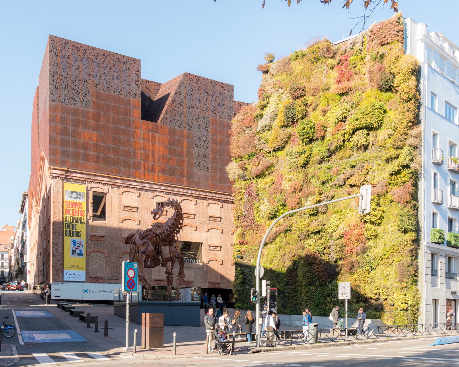 CaixaForum Madrid's rust-colored perforated metal facade beside its vertical garden wall, with the horse skeleton sculpture at the entrance