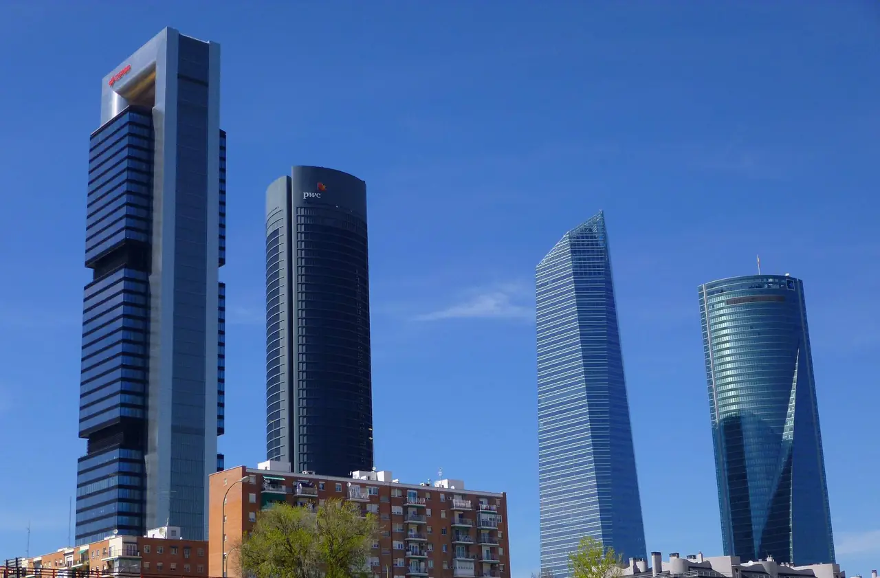 The four skyscrapers of the Cuatro Torres Business Area against a clear blue sky, with apartment blocks in the foreground