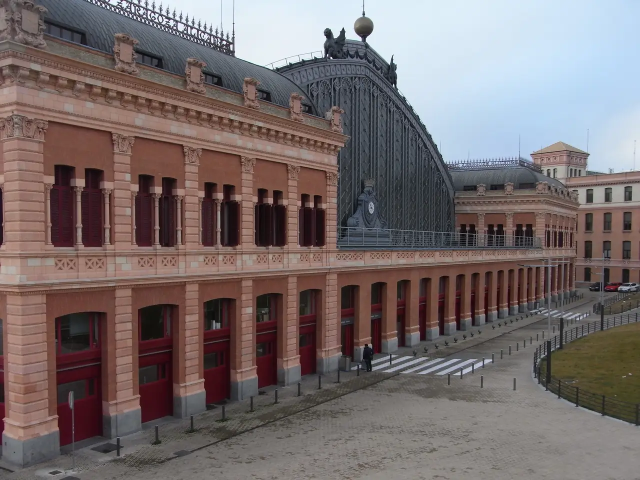 The brick facade and glass-and-iron train shed of Madrid Atocha station, with its clock tower and sculpted griffin