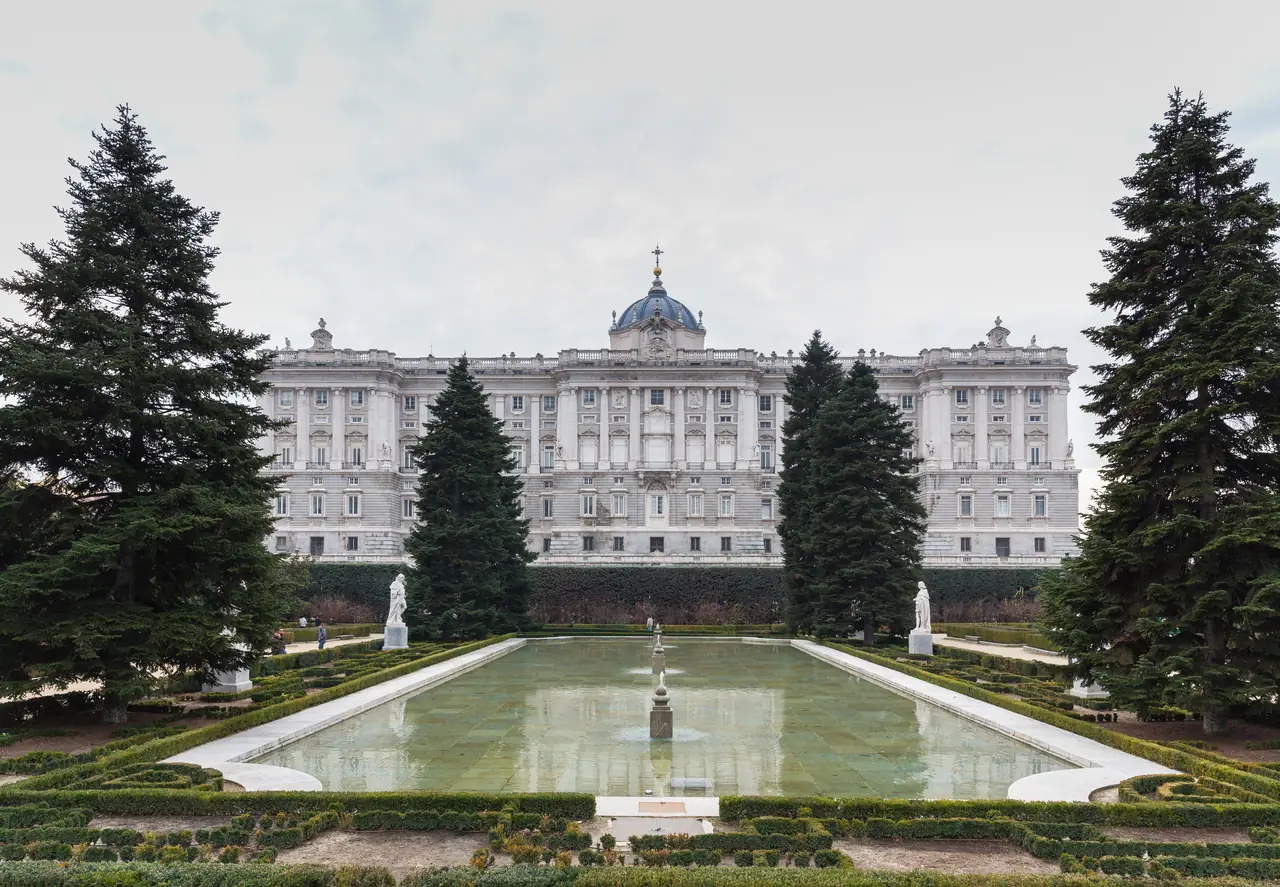 The Royal Palace seen across a formal reflecting pool and clipped hedges in the Sabatini Gardens, framed by conifers