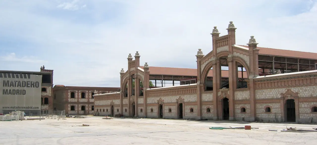 The brick industrial buildings of Matadero Madrid with their arched brick gateways, and the 'Matadero Madrid' sign on the plaza wall