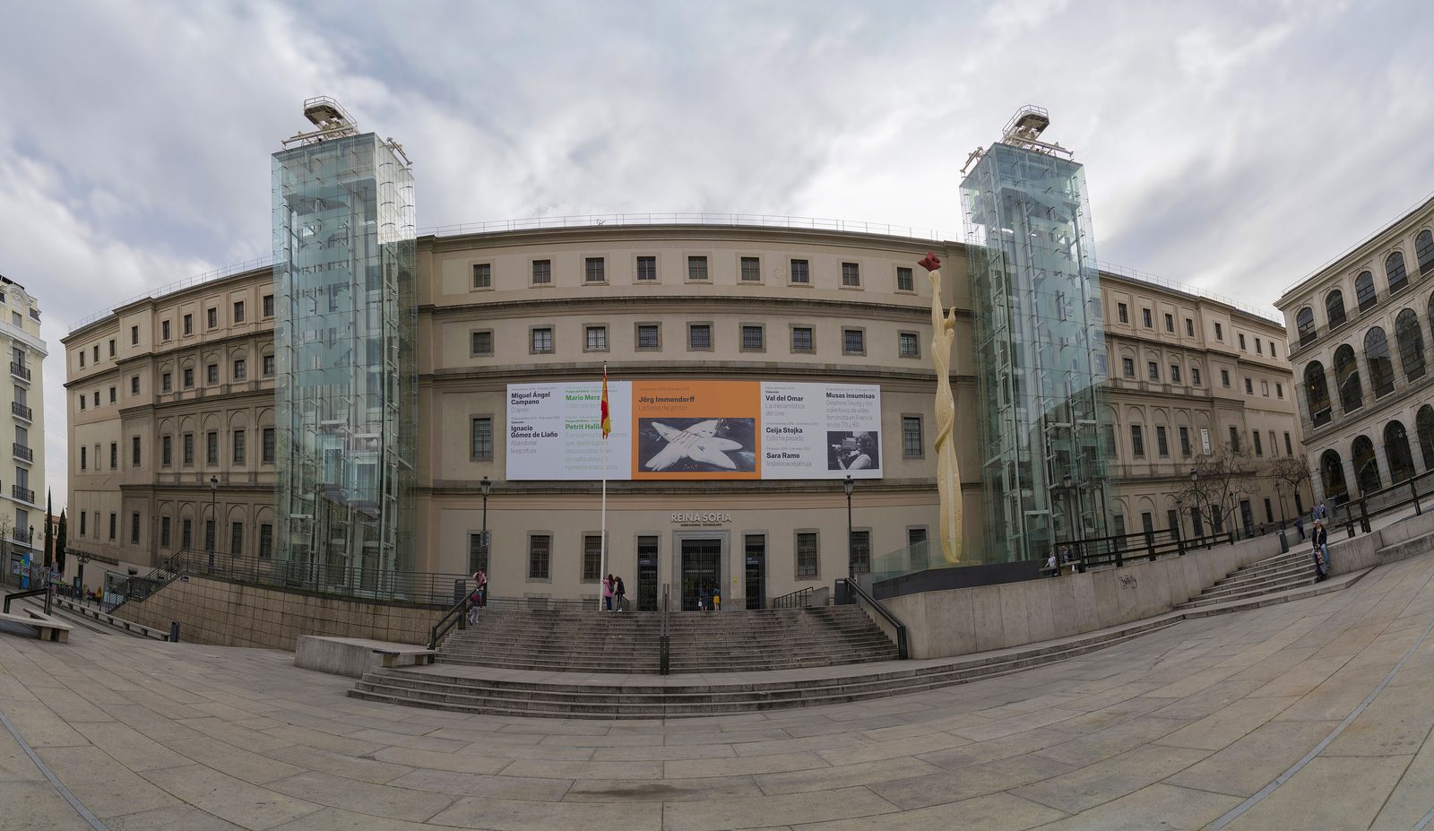 The Sabatini Building of the Museo Reina Sofía in Madrid, its long curved facade flanked by two exterior glass elevator towers rising above the plaza