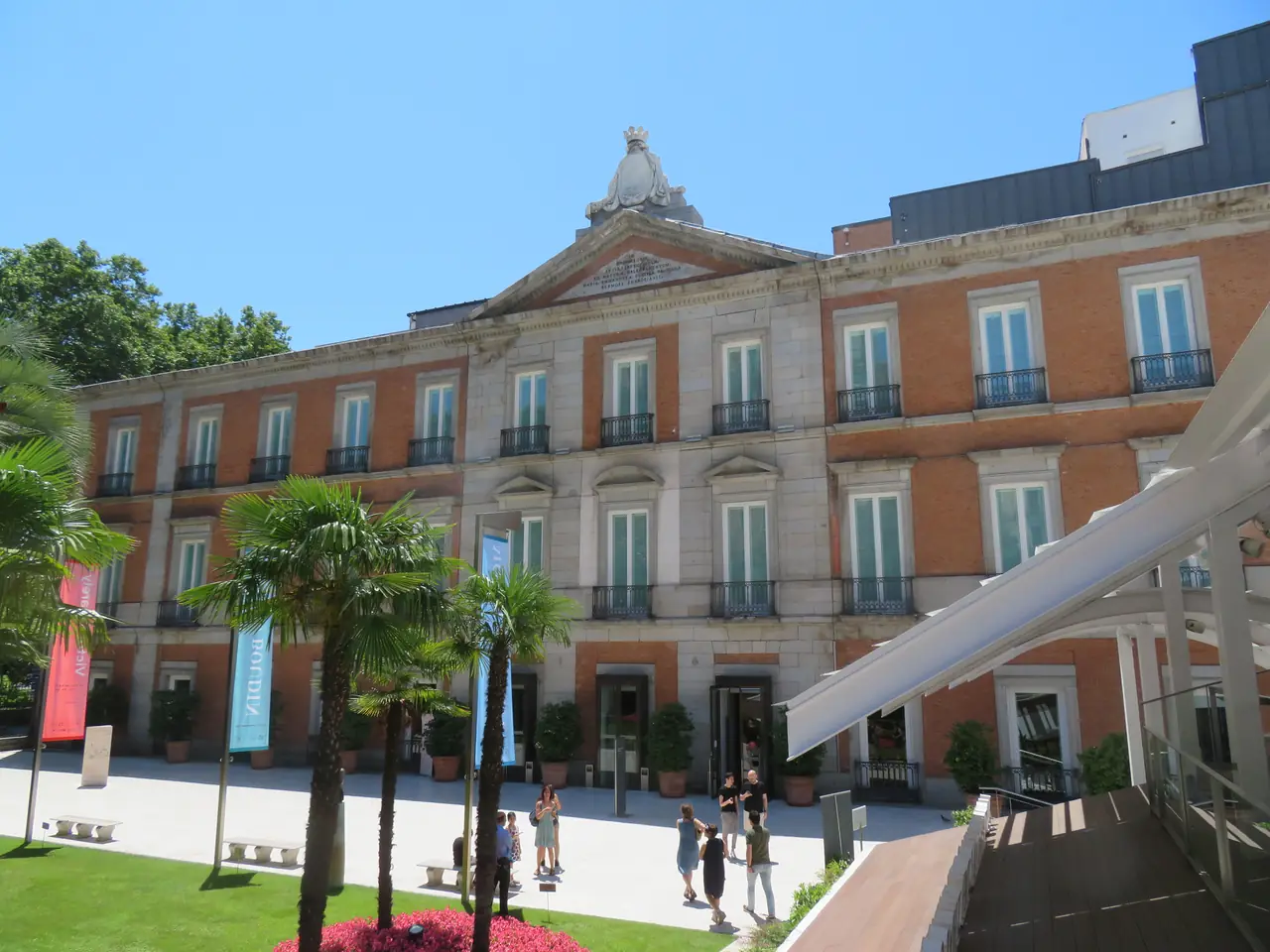 The Palacio de Villahermosa building housing the Museo Thyssen-Bornemisza, with palm trees and exhibition banners at the entrance plaza