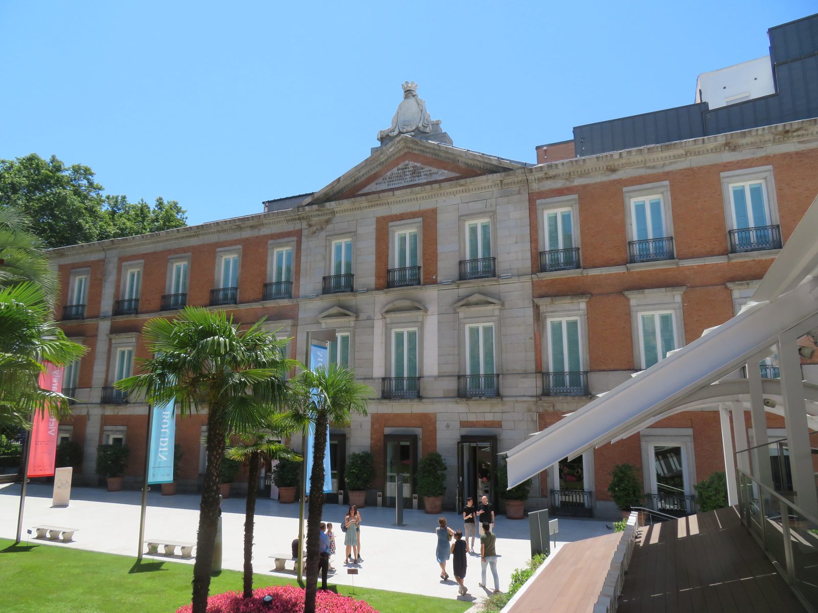 The Palacio de Villahermosa building housing the Museo Thyssen-Bornemisza, with palm trees and exhibition banners at the entrance plaza
