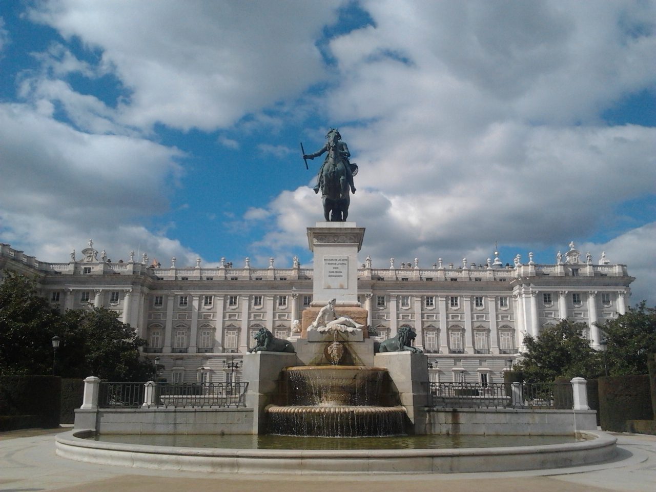 The equestrian statue of Felipe IV in Plaza de Oriente with the Royal Palace's facade behind it under a cloudy sky
