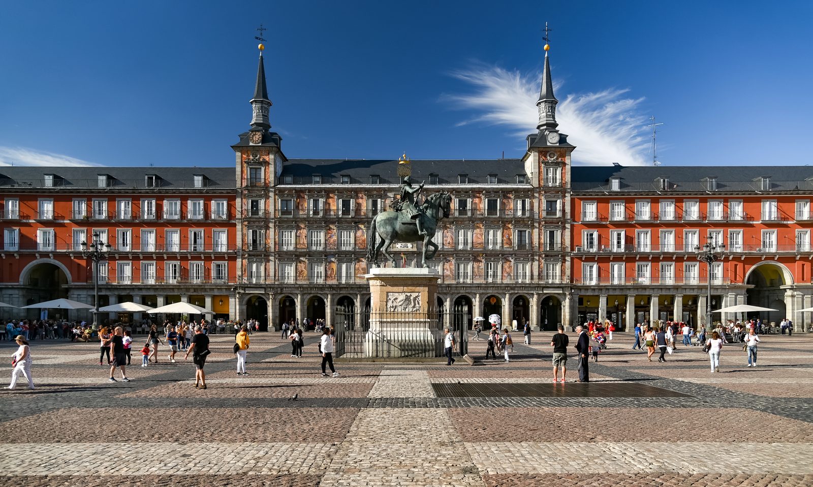 Plaza Mayor's red facades and twin spired towers, with the bronze equestrian statue of Felipe III at the center of the square
