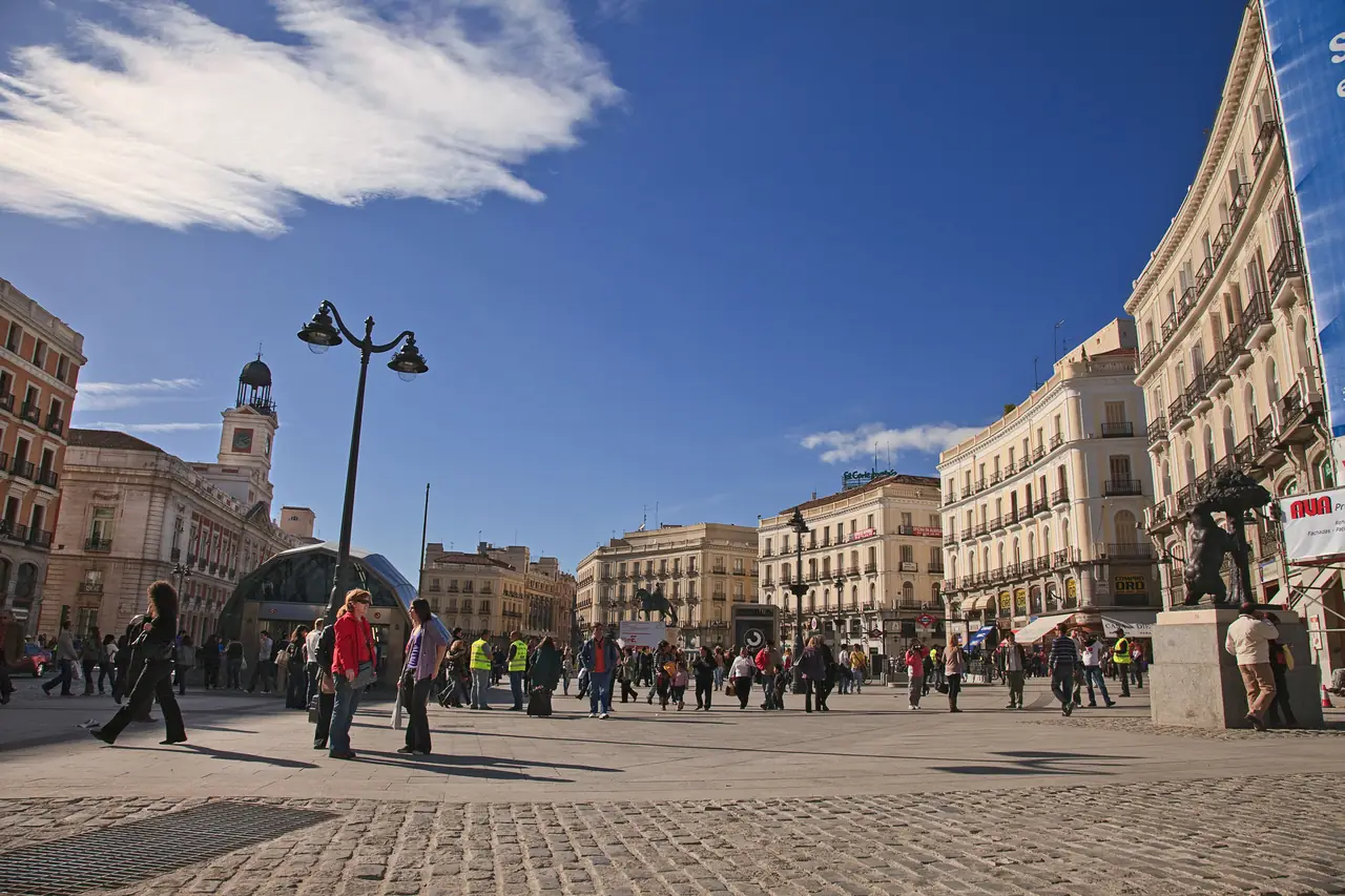 Puerta del Sol plaza with the Real Casa de Correos clock tower on the left and crowds crossing the open square