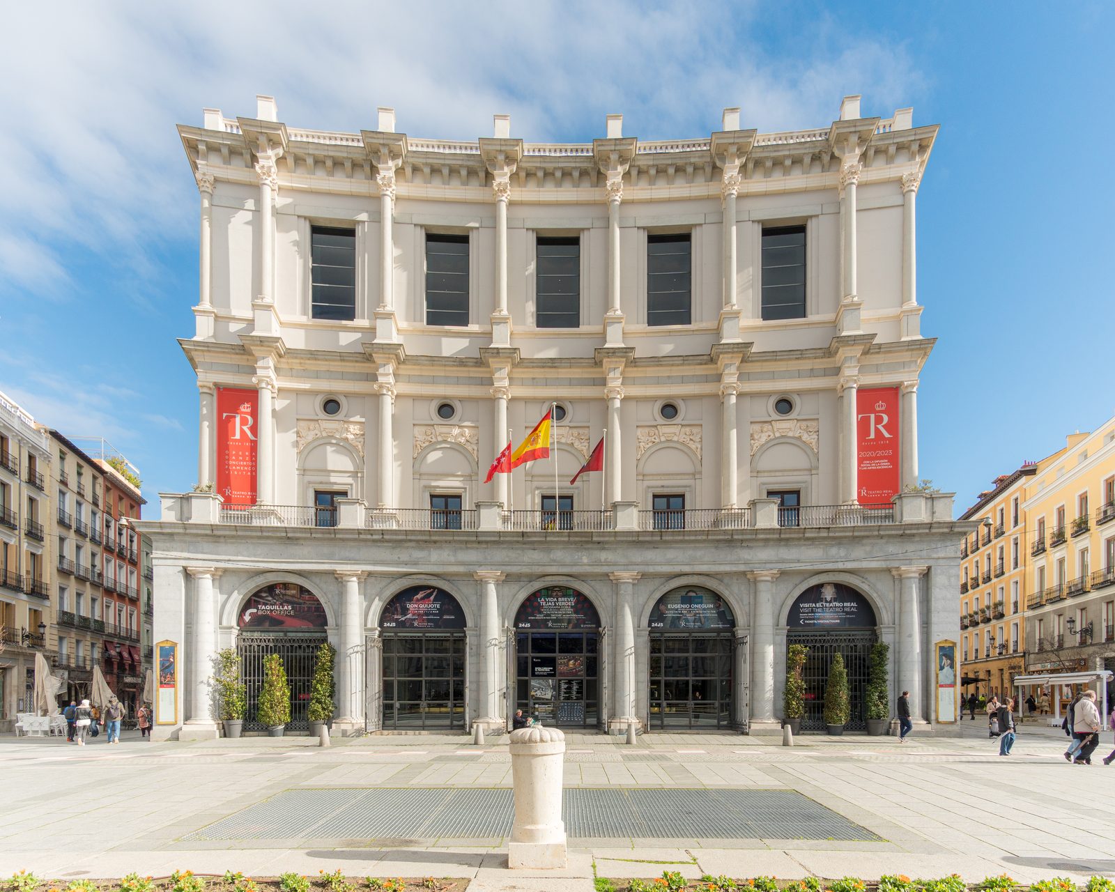 Teatro Real's colonnaded neoclassical facade with red opera-season banners and posters over the box-office entrance