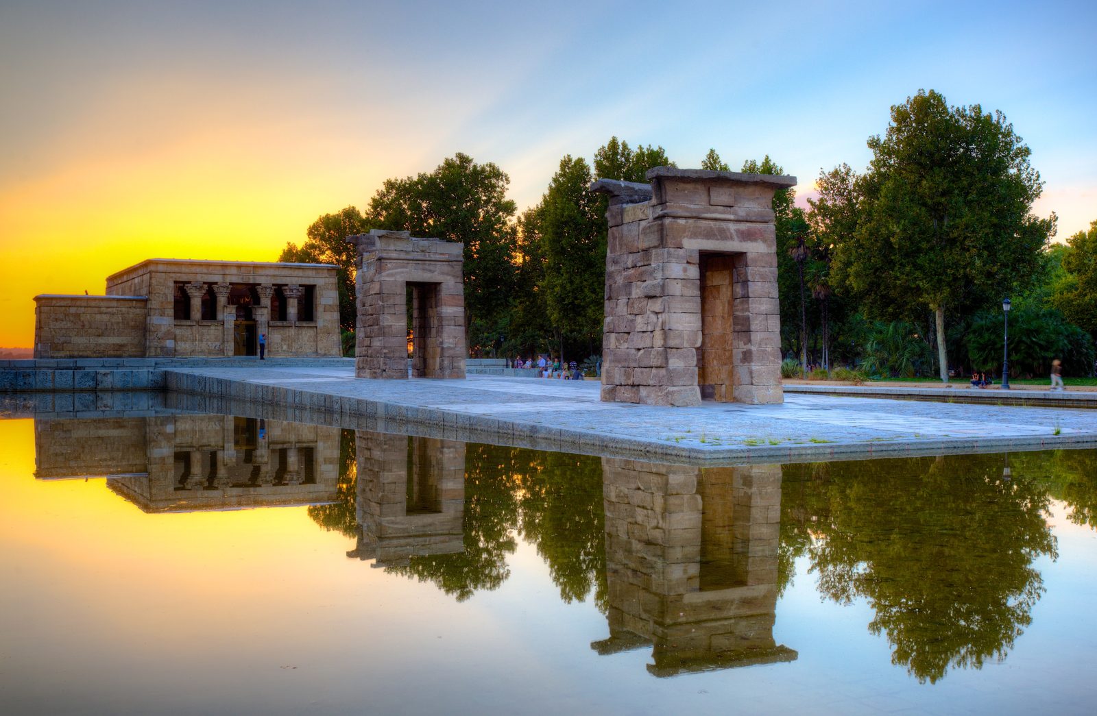 The Templo de Debod's stone gateways and temple building reflected in still water at sunset