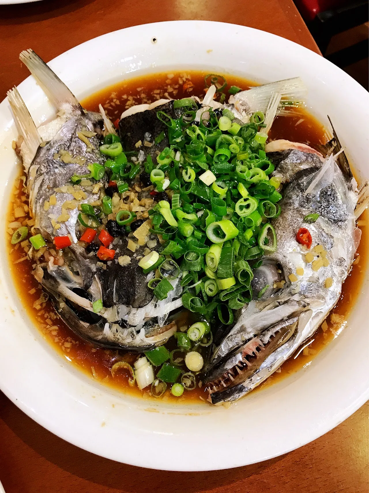 A whole steamed fish topped with scallions in soy broth
