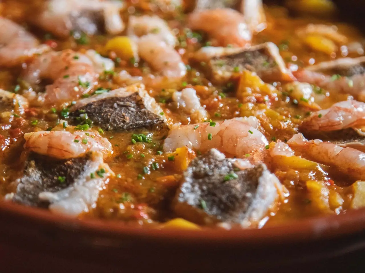 Close view of a seafood and cod stew with prawns, fish pieces and chives in a terracotta dish