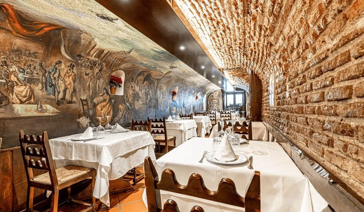 A dining room with a painted mural on the wall and a curved brick ceiling above set tables.