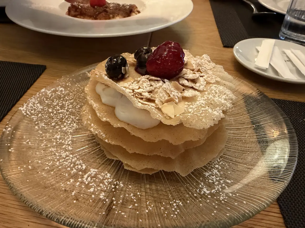 Layered mille-feuille dessert with cream, almond flakes, powdered sugar and berries on a glass plate