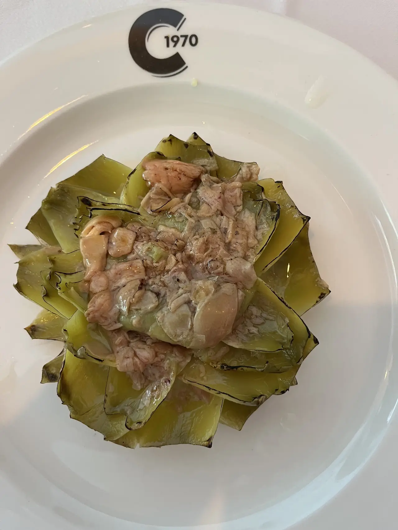 Roasted artichoke leaves topped with sauteed mushrooms and meat on a branded plate
