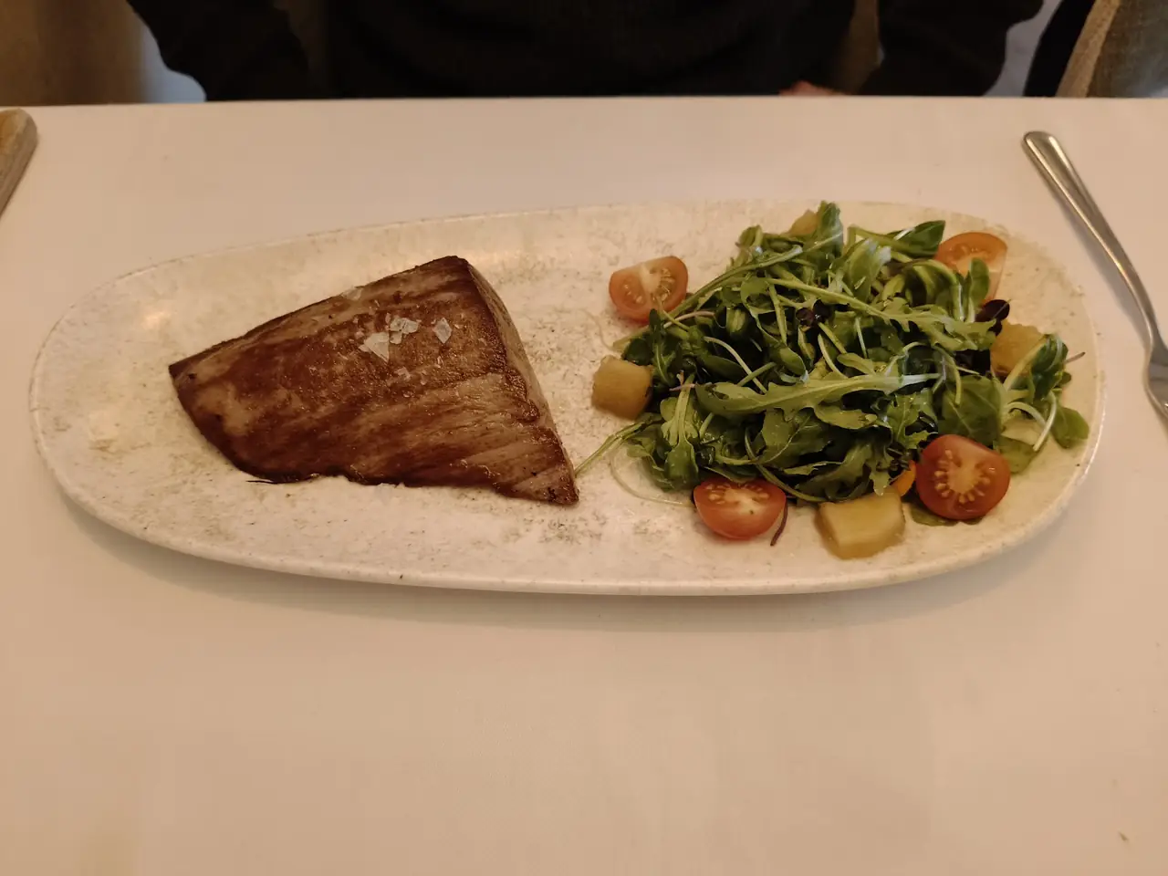 Seared tuna steak with sea salt beside an arugula and cherry tomato salad on an oval plate
