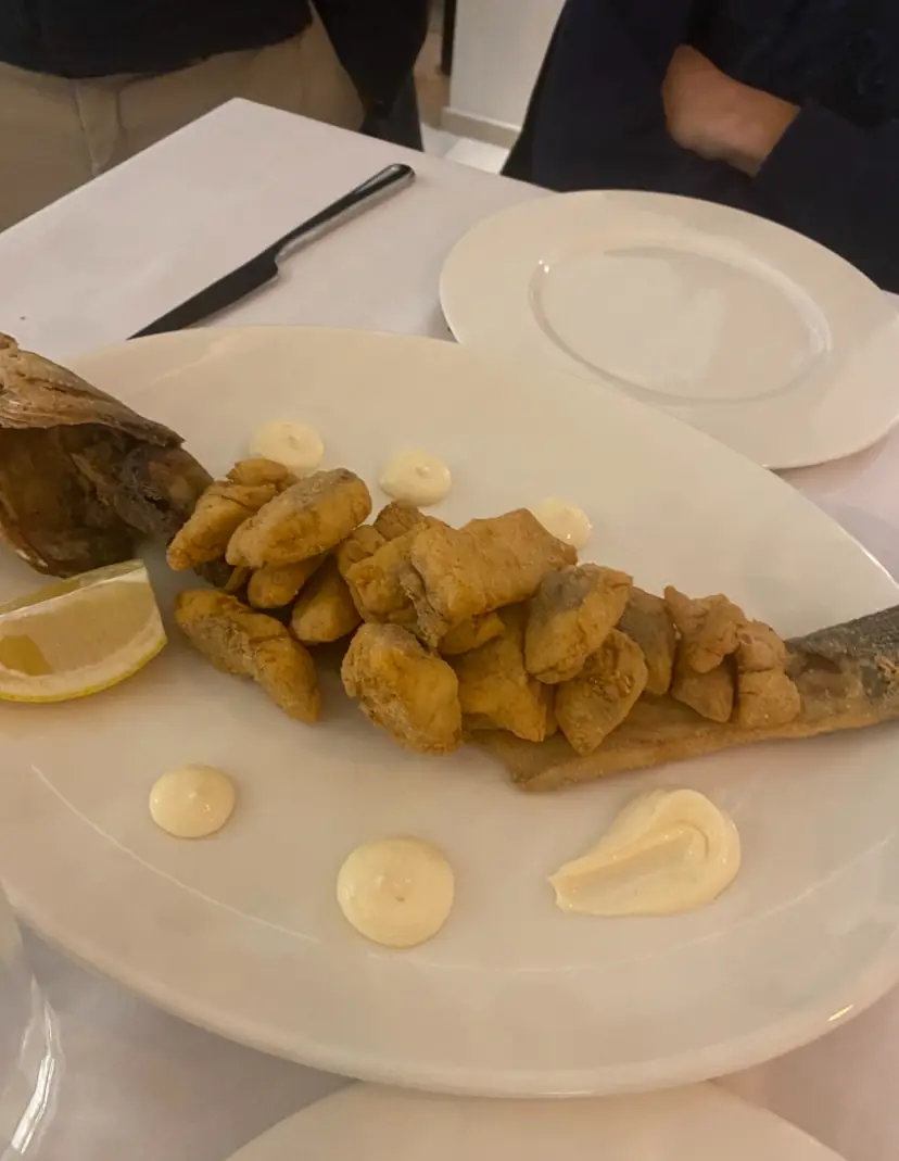 Fried fish pieces plated over whole fish skeleton with aioli dots and a lemon wedge