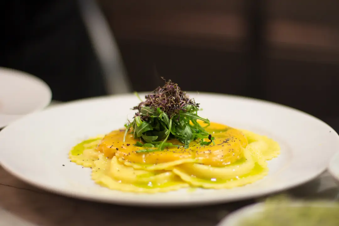 Egg yolk ravioli topped with arugula and microgreens on a white plate, drizzled with green oil, Las Fernández.