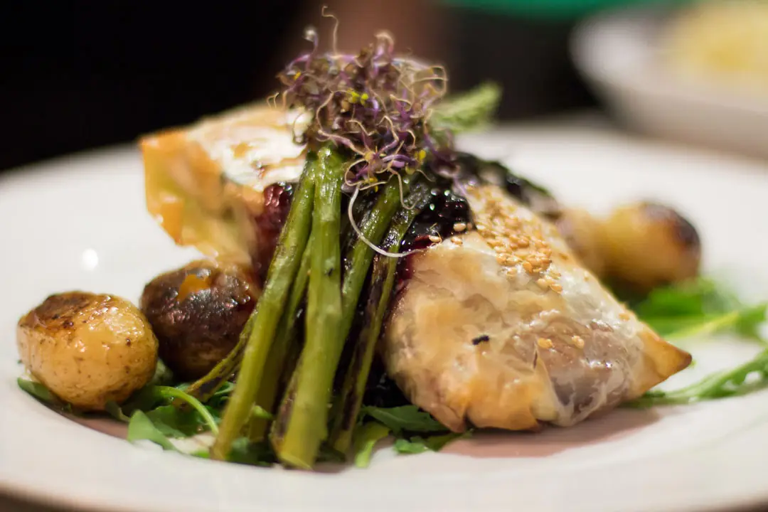 Golden filo pastry parcel with berry sauce, roasted baby potatoes, asparagus, and sprouts on a white plate, Las Fernández.