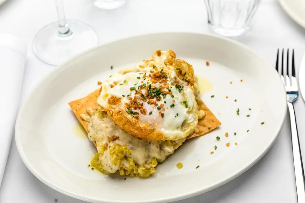 Fried egg over creamy leek and potato with crispy garnish on a white plate