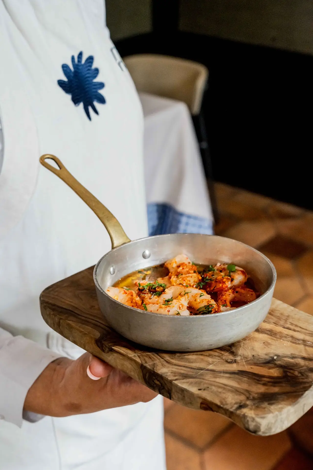 Garlic shrimp served in a small metal pan on a wooden board, being carried to the table