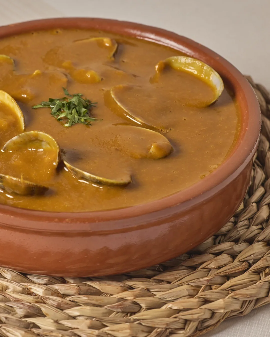 An earthenware dish of clams in an orange broth