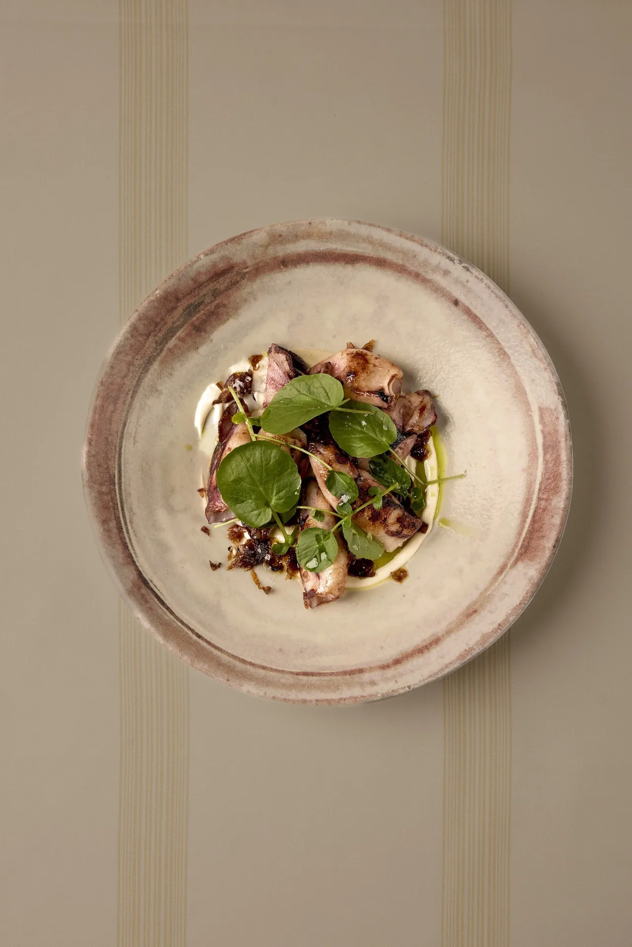 A small dish with dark leaves and morsels on a round plate