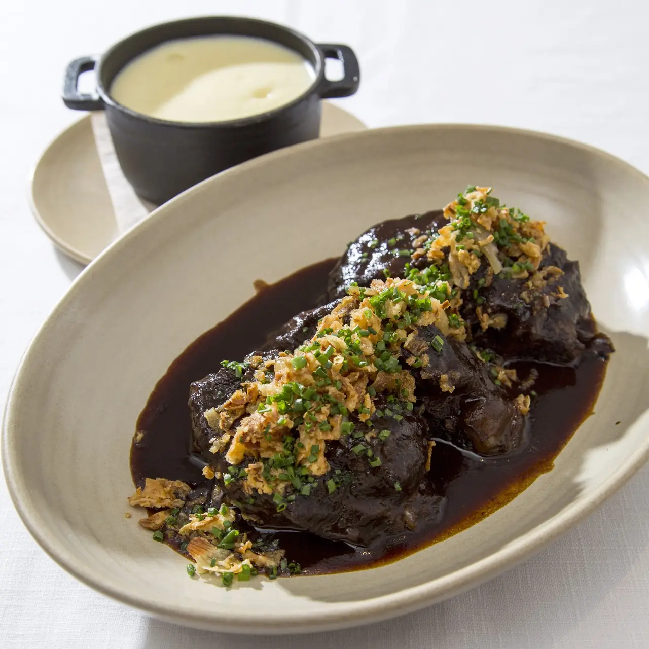Braised meat in dark sauce topped with crispy onions and chives, with a side of potato puree