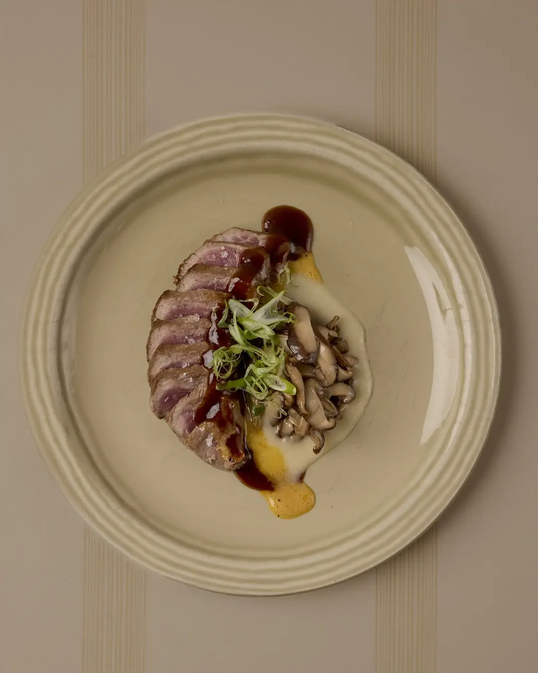 Sliced pink meat plated with sauteed mushrooms, scallion and dark and cream sauces on a round plate