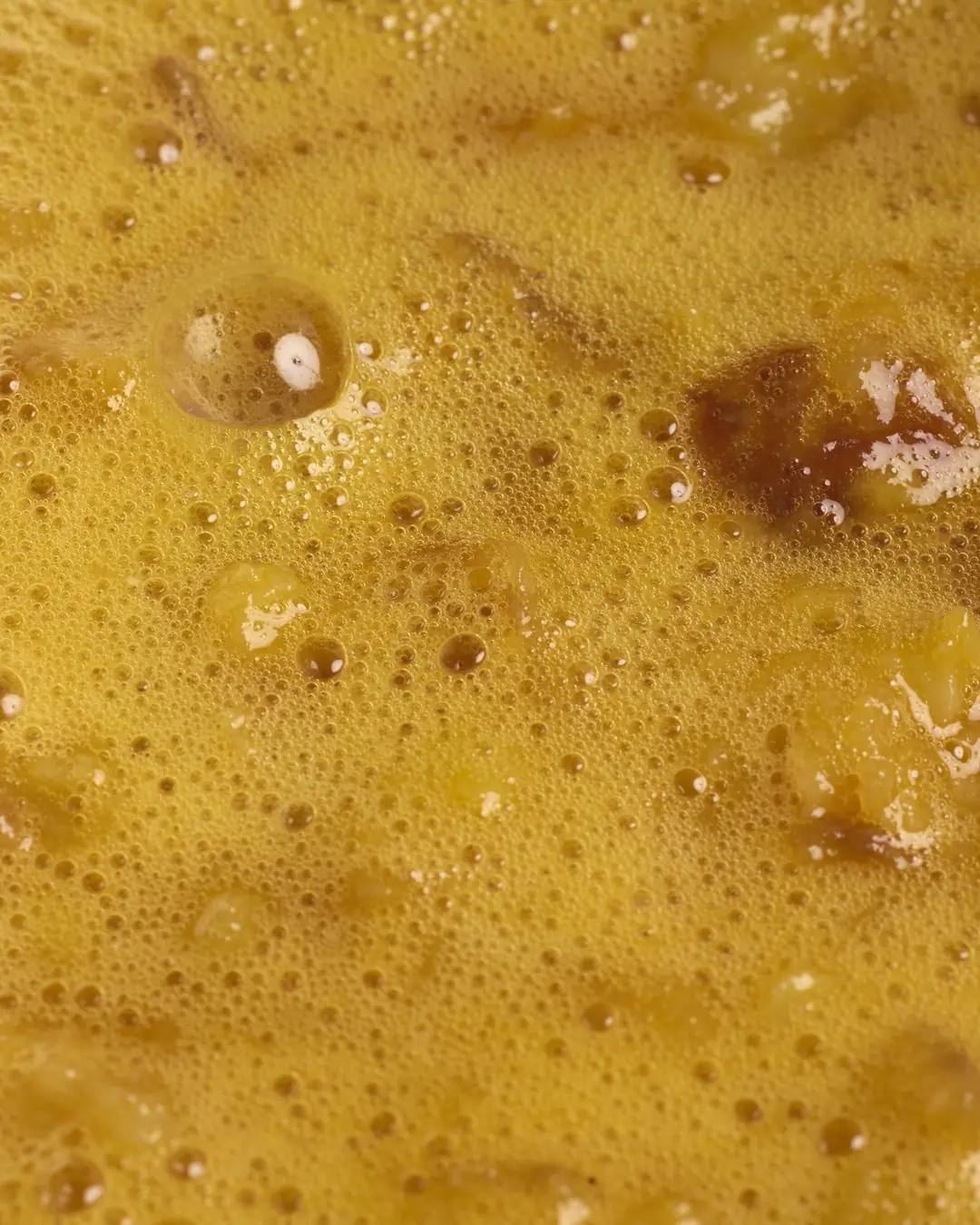 Extreme close-up of a glossy golden egg surface with small bubbles and browned edges