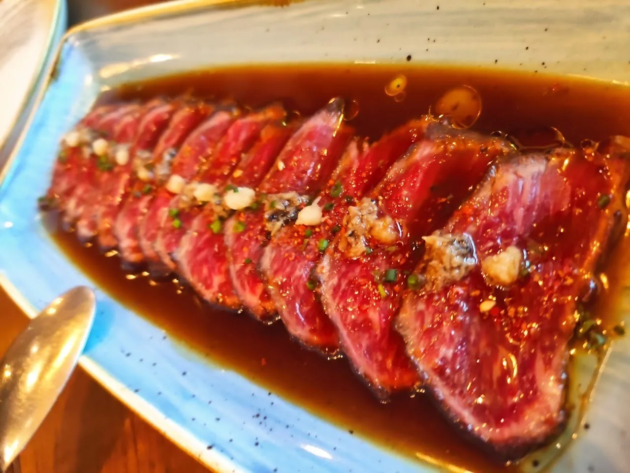 Thin slices of seared meat in dark sauce on a blue plate